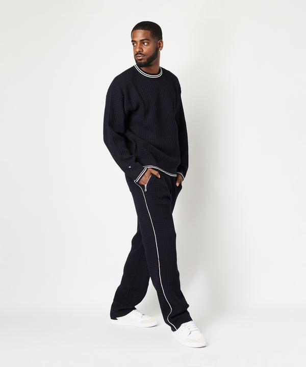 CUSTOM_ALT_TEXT: Side view of male model wearing Paper Planes Racked Rib Sweater and Pant, color Parisian Night.