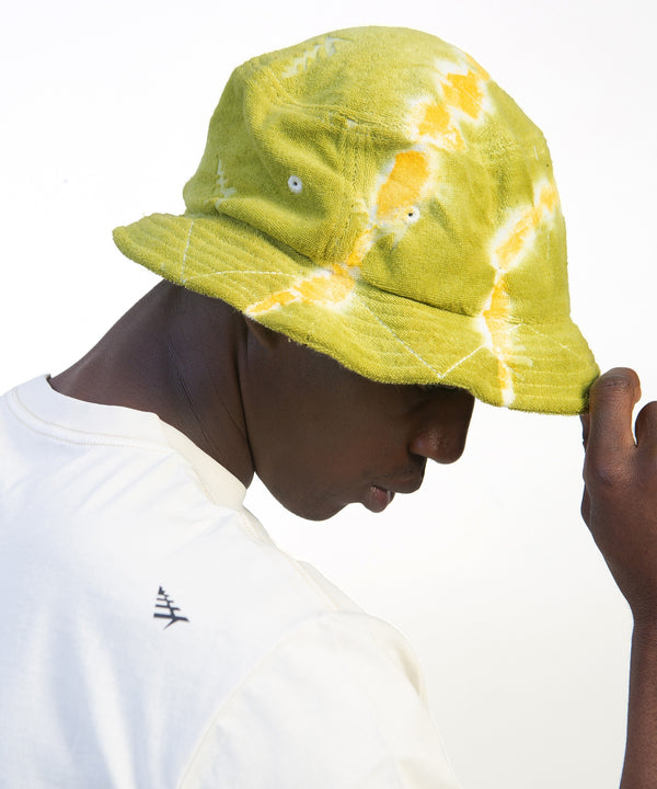 CUSTOM_ALT_TEXT: Male model wearing Paper Planes Tie Dye Jacquard Terry Cloth Bucket Hat color Olive.