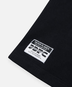 CUSTOM_ALT_TEXT: Woven jacquard patch on Paper Planes PDFC Oversized Tee, color Black.