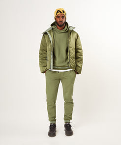 CUSTOM_ALT_TEXT: Model model wearing Paper Planes Puffer Jacket and Logo Jacquard Hoodie and Pant, color Bronze Green.