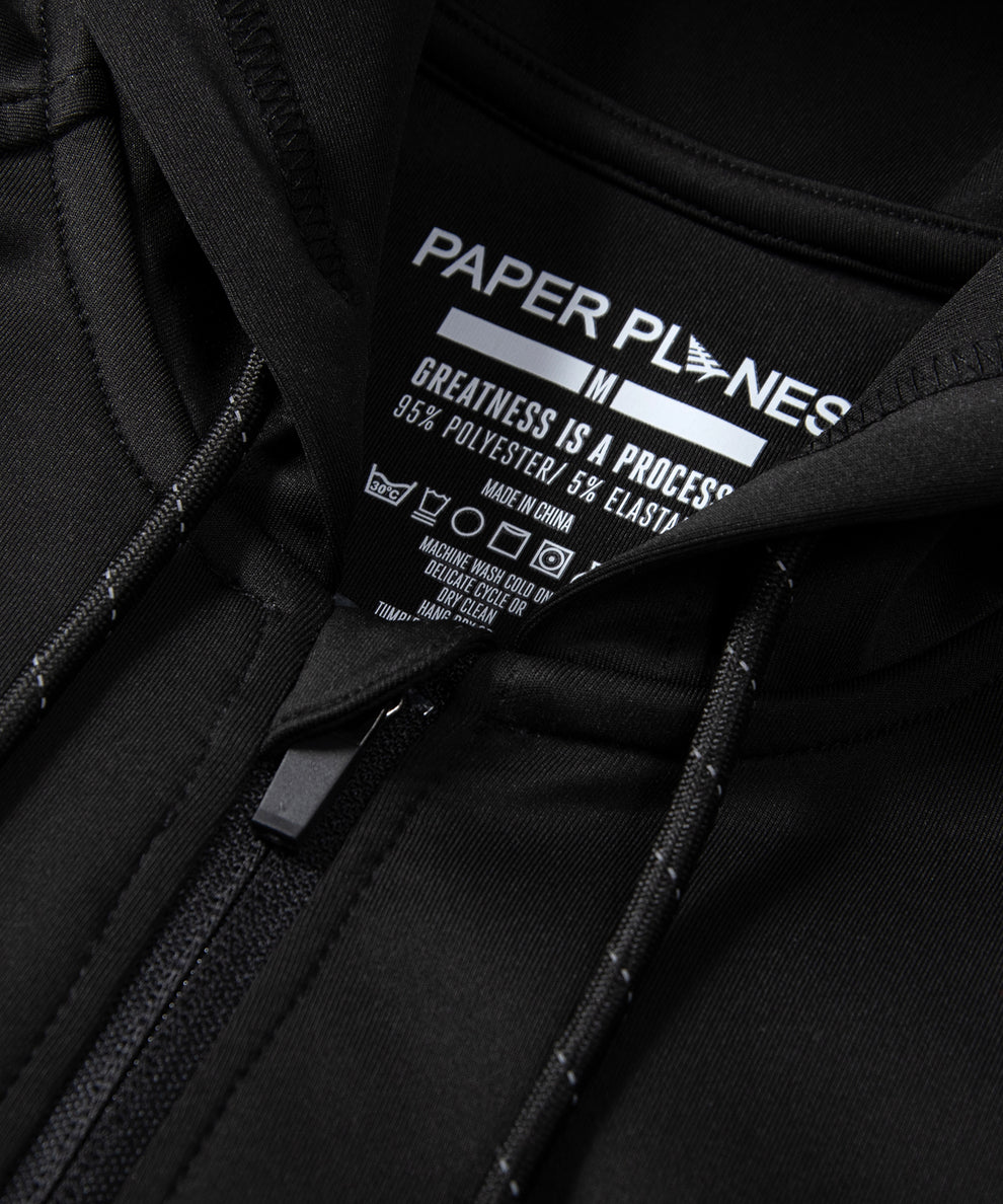 CUSTOM_ALT_TEXT: Neck opening detail with reflective drawcord on Paper Planes Greatness Is a Process Zip-Up Hoodie, color Black.